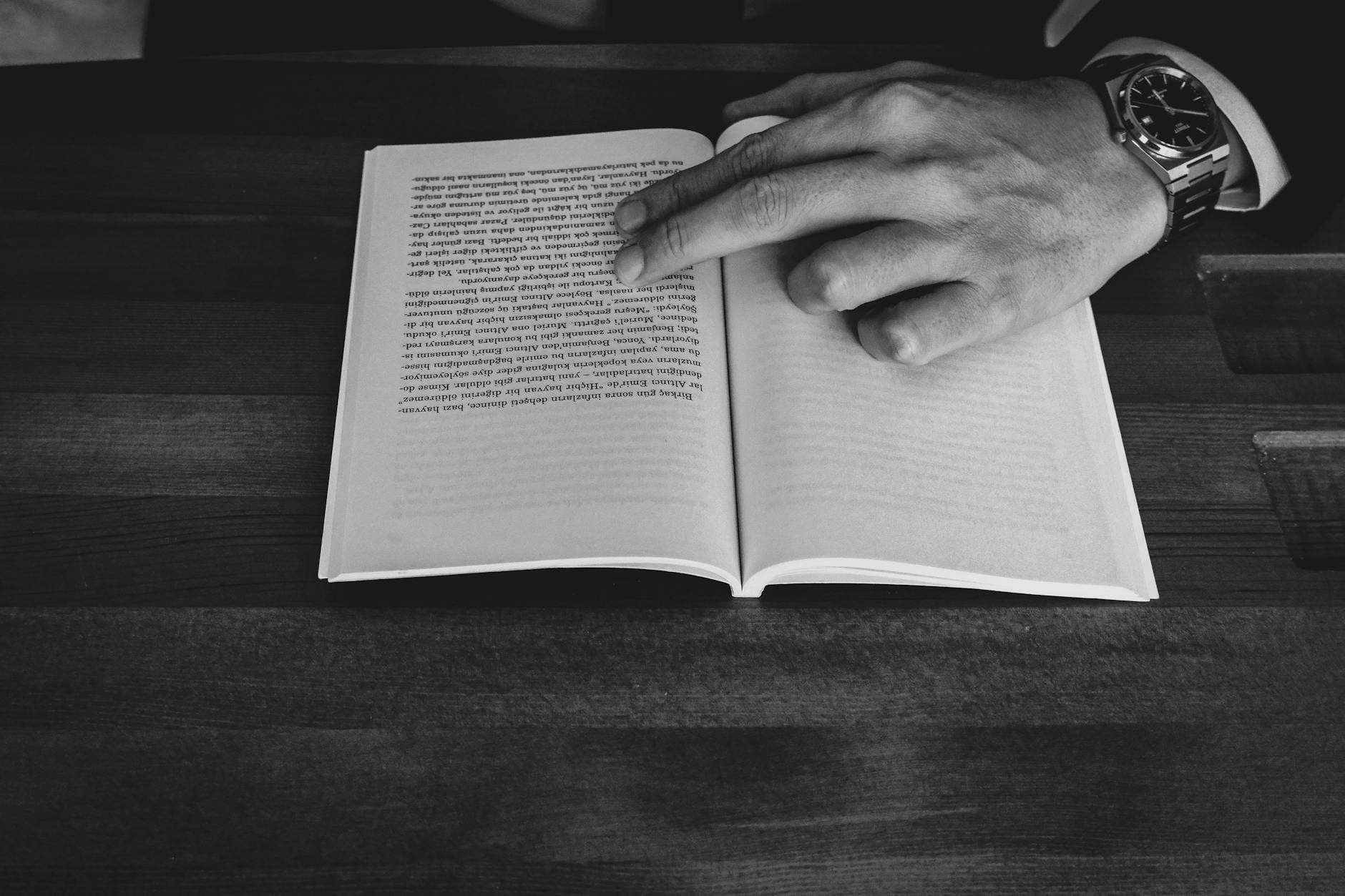 Męska dłoń wskazuje fragment książki leżącej na drewnianym stole